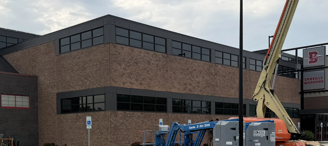The same school corner after staining, the tan brick now one even brown, the lifts still parked in the lot