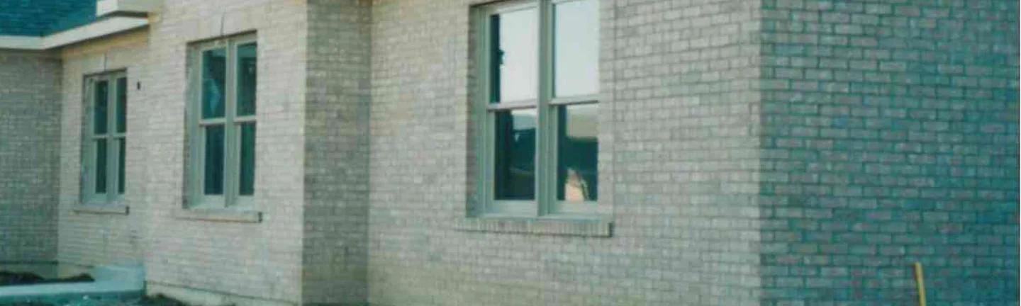 A band of the buff brick wall of the Dayton house in October 1998, windows with grey frames under a dark shingled roof, the units one even range