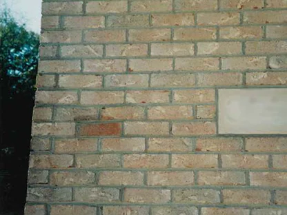 A close-up of the buff brick in 1998 before the work, one dark red brown unit standing out from the wall beside a hose bib