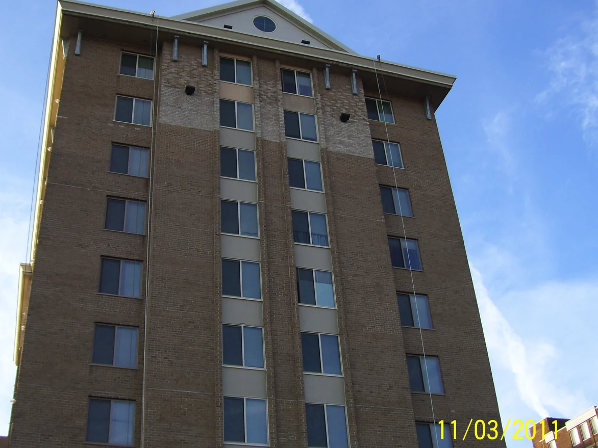 The apartment building from below in 2011, its brick brown-tan at the base and running through a wide band of paler units across the upper floors, under a pedimented gable