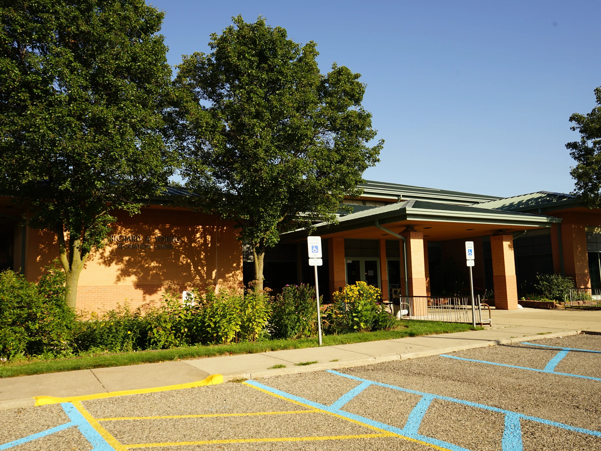 The recreation center from its parking lot in 2019, the same name wall and the entrance canopy in warm red and tan brick under mature trees