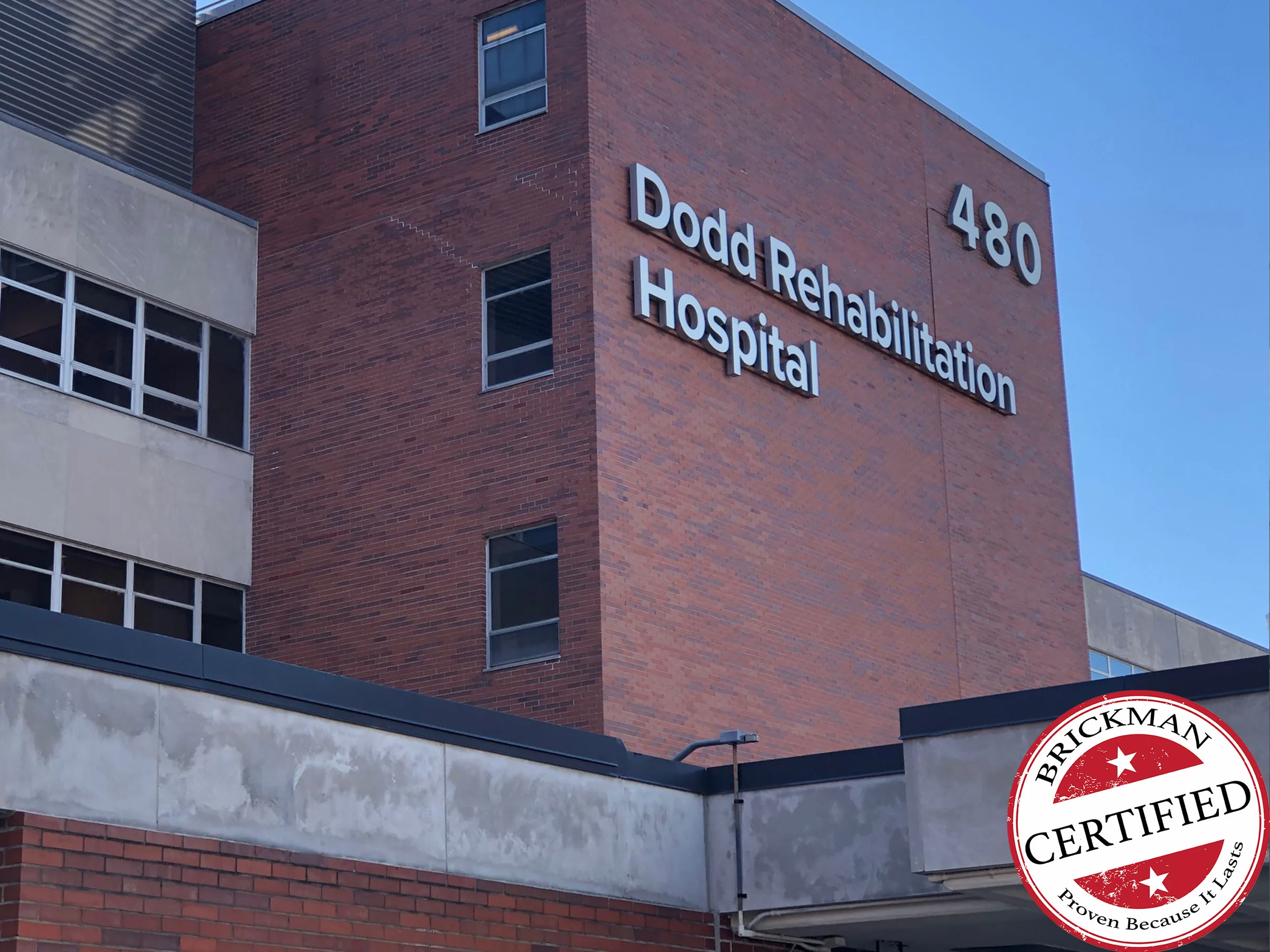The same brick block in 2021 under a clear sky, one red range from the canopy to the parapet with Dodd Rehabilitation Hospital and the number 480 in metal letters, and the certification stamp in the corner