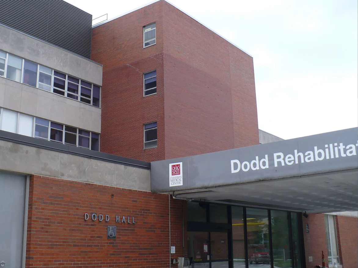 The hospital entrance before the work, a four storey red brick block rising above the canopy beside a grey precast wing, with DODD HALL lettered on the lower wall