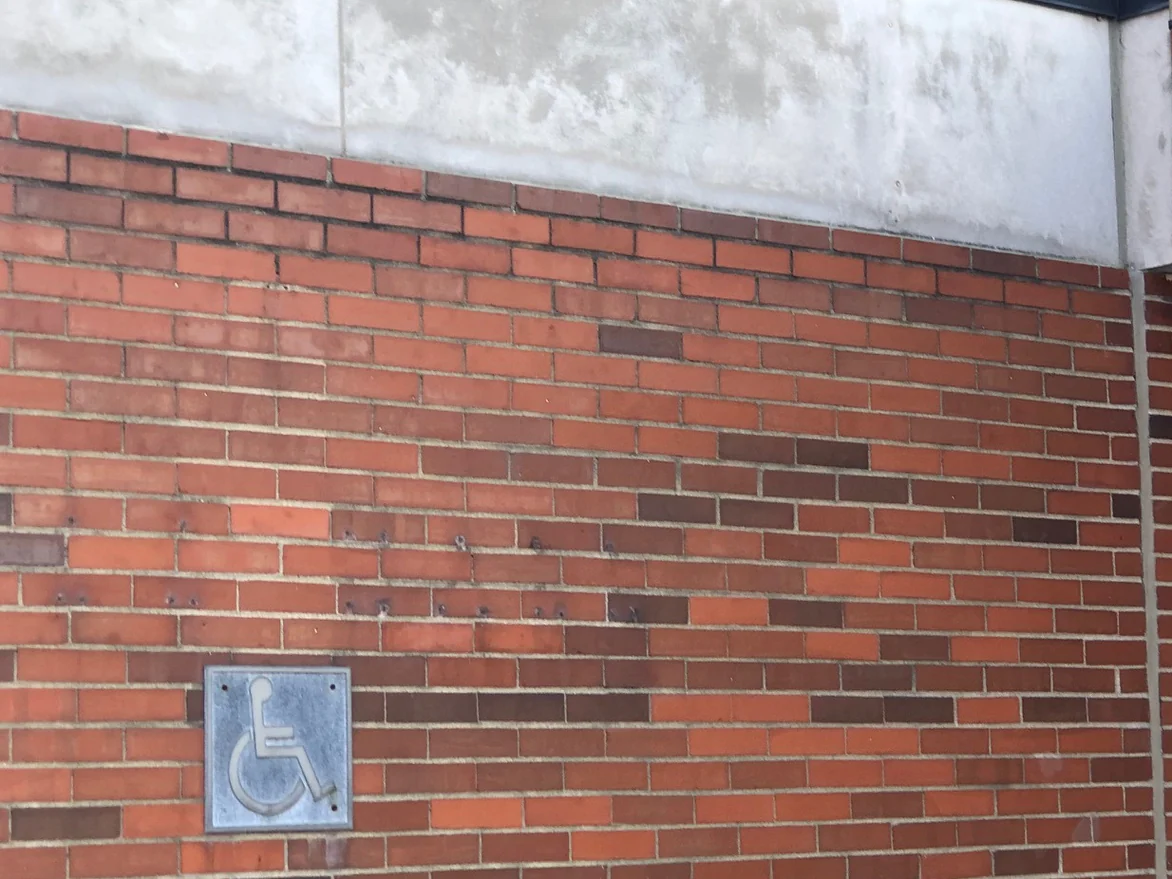 The low entrance wing in 2021, ground level brick in a red and orange range under a precast band, with an accessible plaque set into the wall