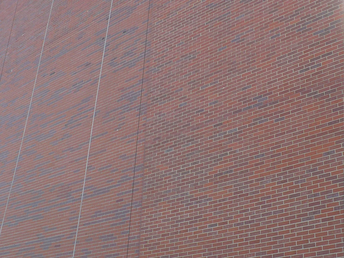The upper wall after the work, two brick fields either side of a control joint reading as one red range with the same scattered grey headers running through both