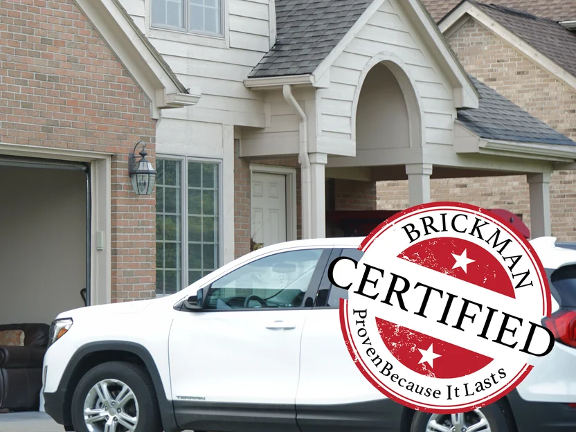 The covered front entry in 2019, red brick running from the garage return to the porch, the frame carrying the Brickman Certified stamp