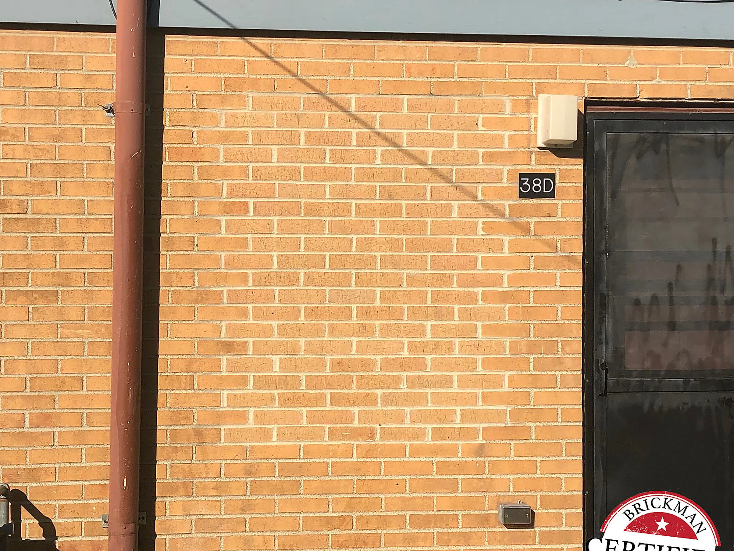 A long run of wall in 2019 next to a service door, the brick even from end to end, the frame carrying the Brickman Certified stamp