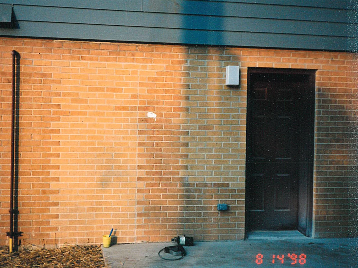 A brick wall beside a dark service door in 1998, blocks of grey filled-in brick and mortar standing against the warm orange brick around them