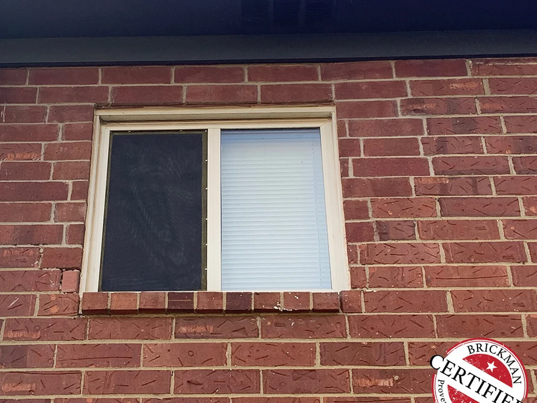 Close view of the same window in 2019, the sill course and the brick on both sides of the opening reading as one red range, with the Brickman certified stamp in the corner of the frame