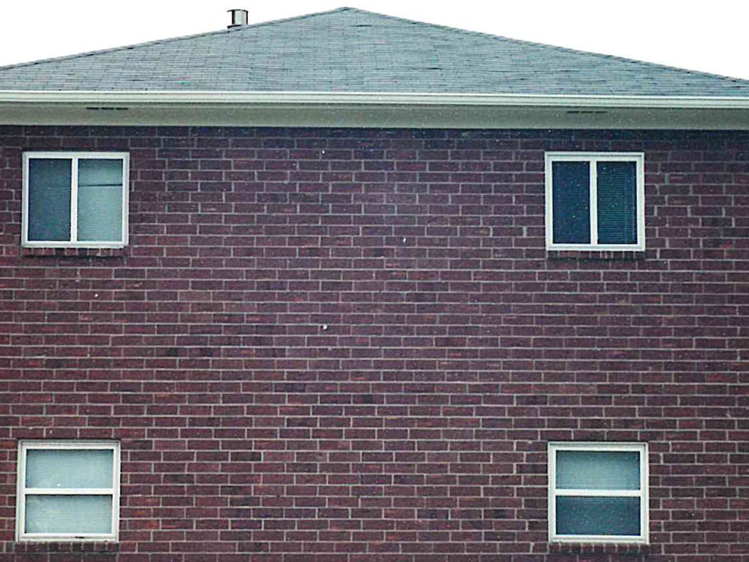 The gable end of the two-story apartment block in 2000, four windows set in dark maroon brick under a hipped roof