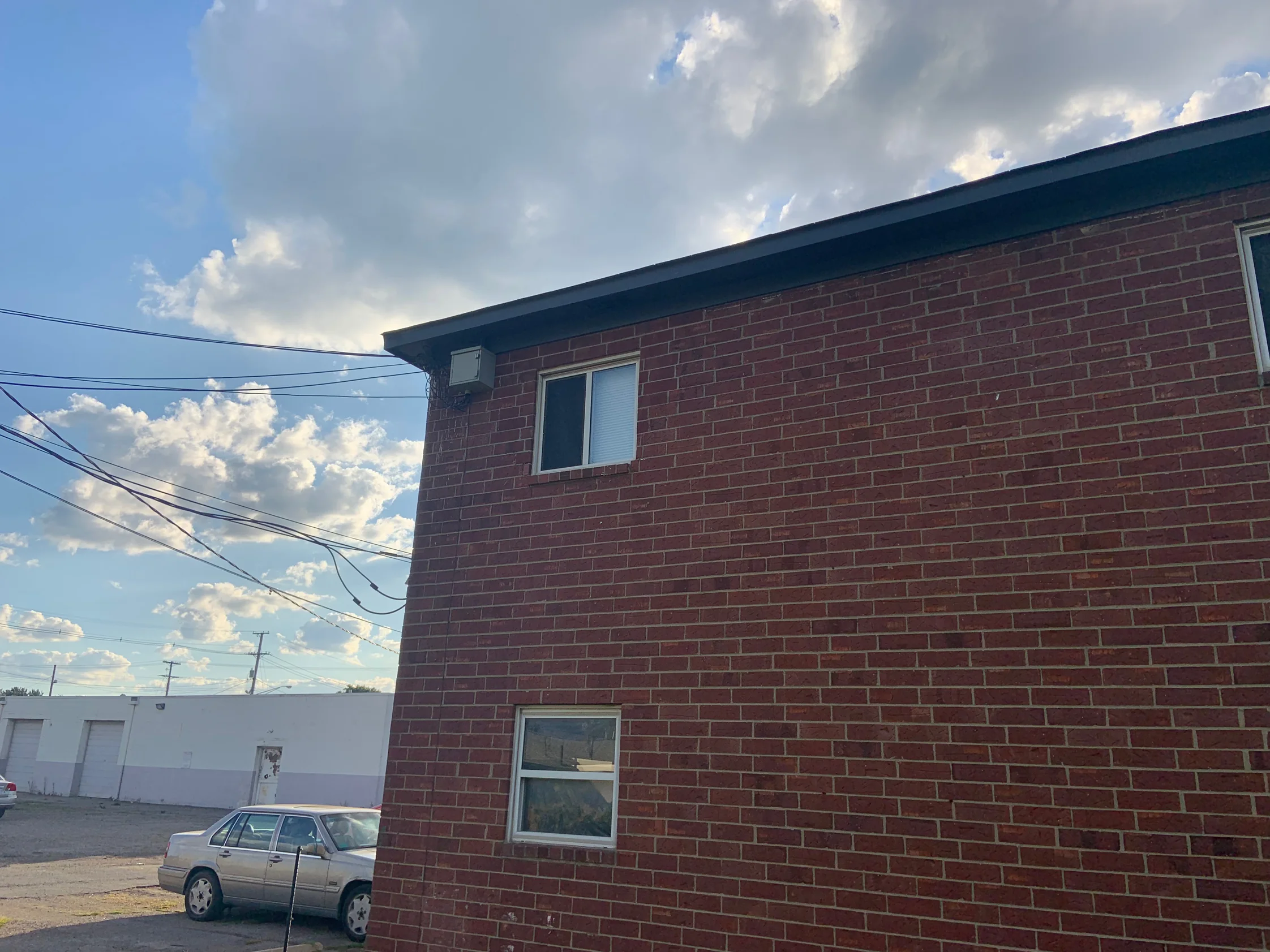 The far gable end of the apartment block in 2019 from the parking lot, a broad red brick wall running up to the roof line under open sky