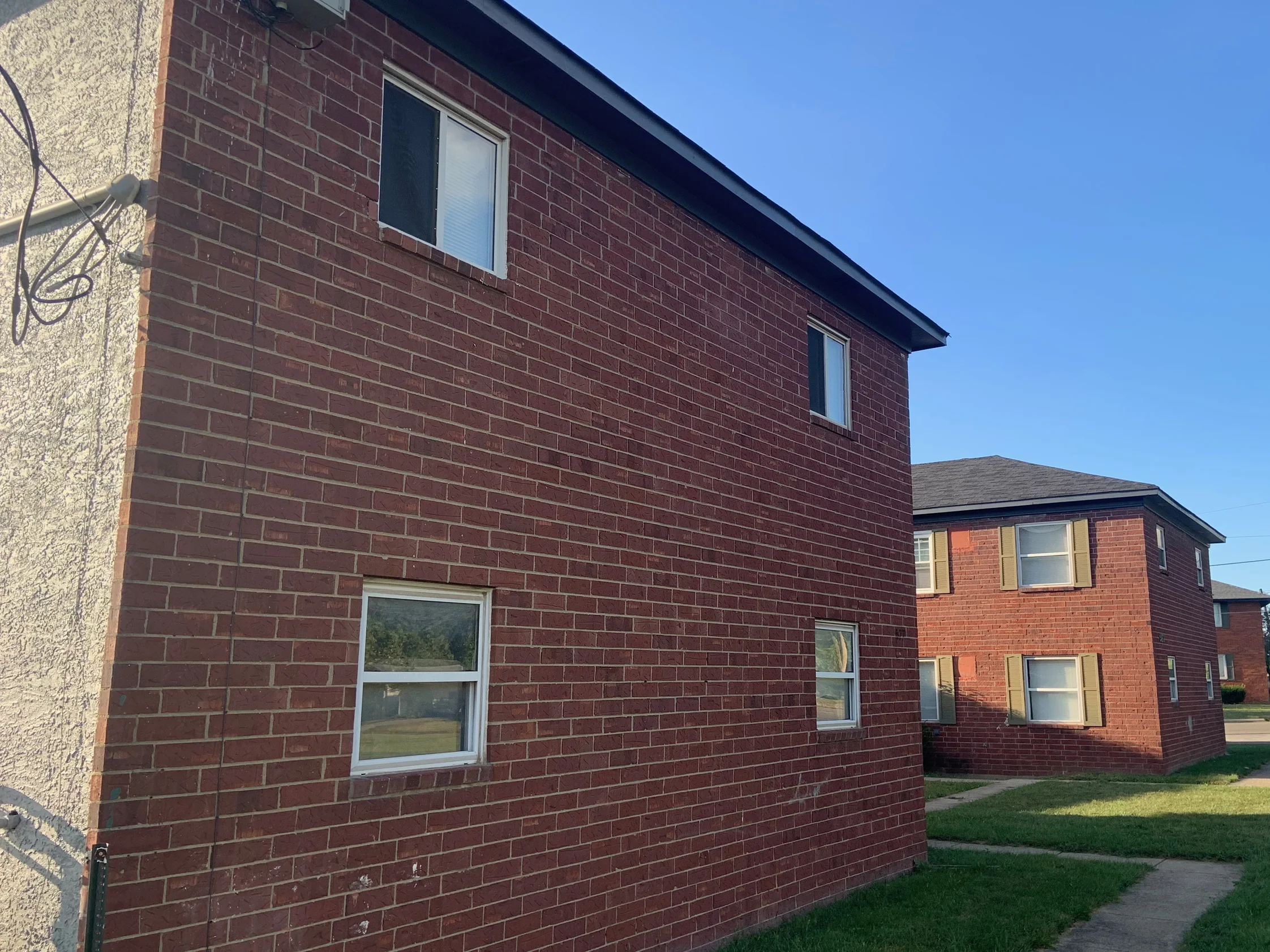 The apartment block along its gable end in 2019, the wall carrying one red range from the eaves to the grass, with a second block and the lawn walkways beyond it