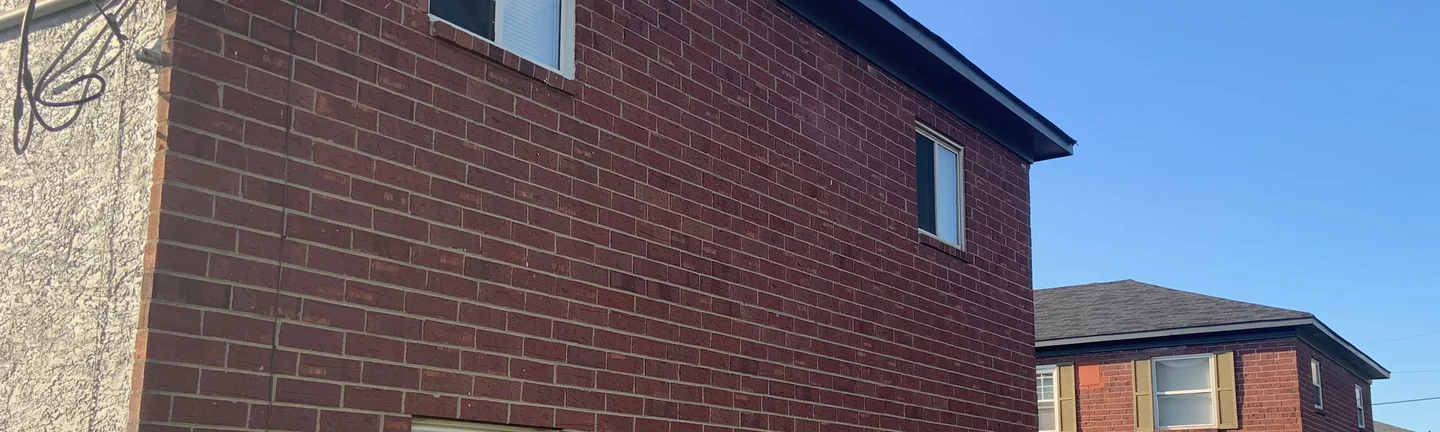 The gable end of a two-story brick apartment block in 2019, a second block and the lawn walkways behind it