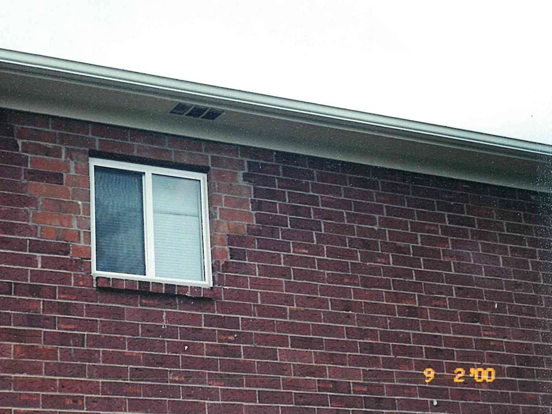 The upper wall of the apartment block in 2000, the brick around and above one window in lighter red and orange units against the dark maroon field beside it