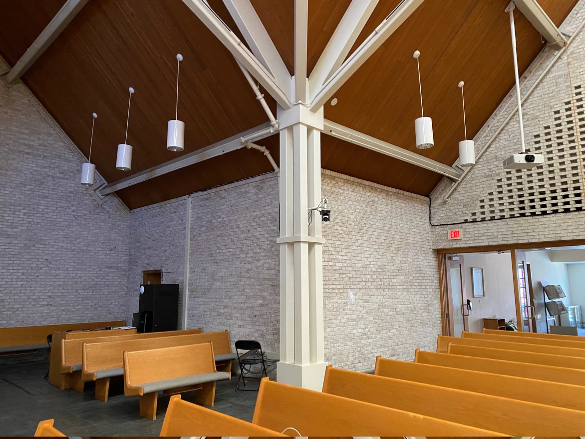 The corner of the hall in 2021 where the side wall meets the screen wall, one cream range across both, a painted column carrying the roof beams and the lobby doors beyond