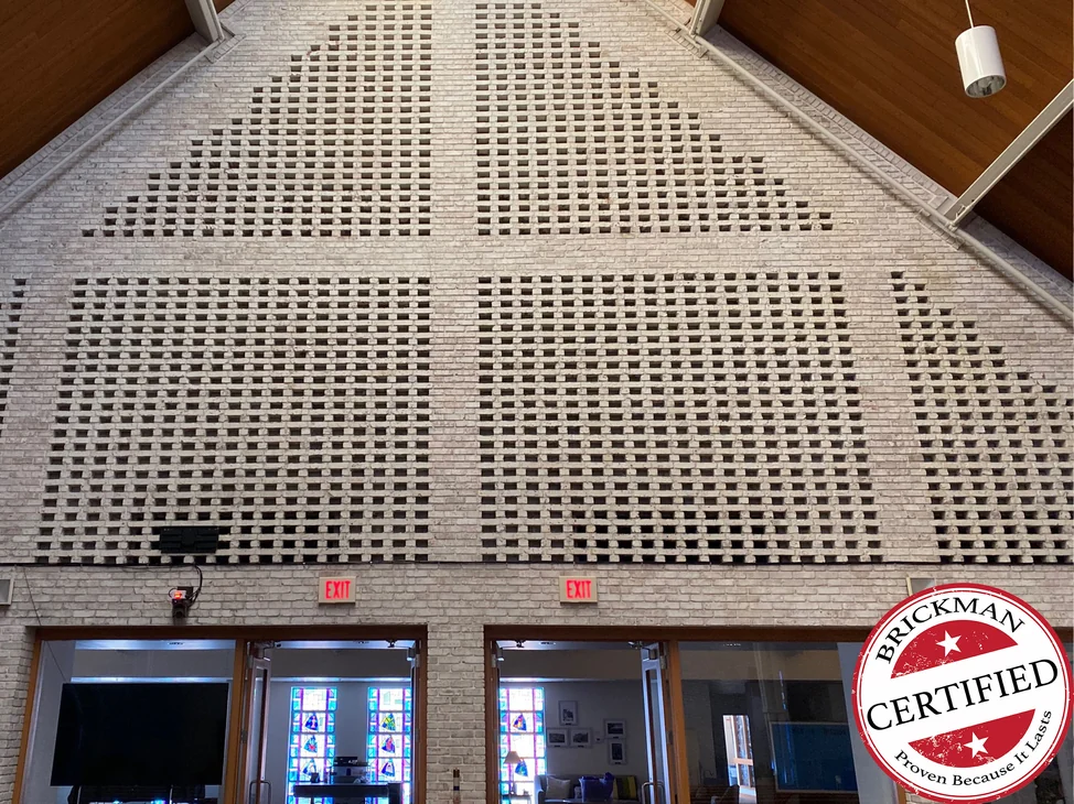 The gable end of the hall in 2021, one range of cream brick across the pierced screen wall above two pairs of doors, with the certification stamp in the corner.
