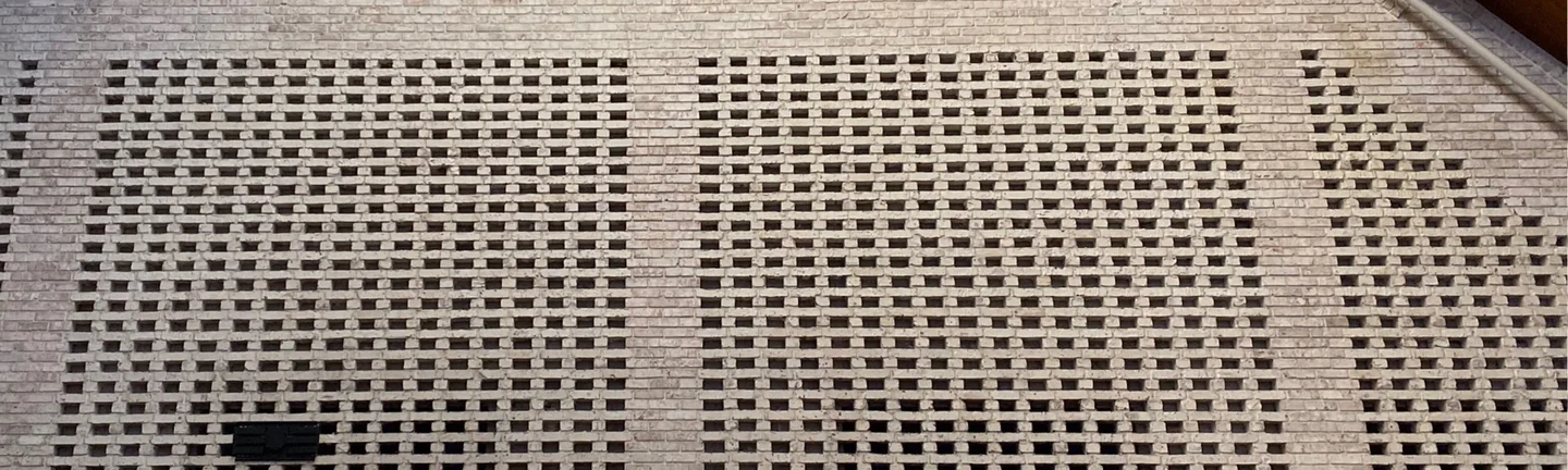 The pierced brick screen wall inside the Elmhurst church in 2021, one range of cream brick under a wood ceiling