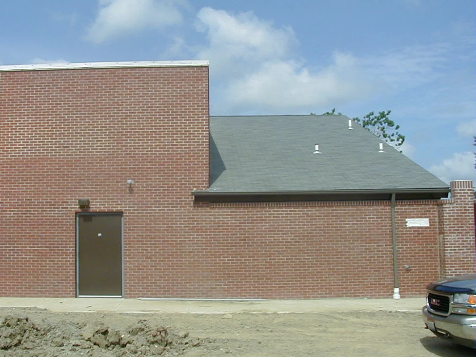 The same side wall of the restaurant in 2003 after staining, the tall elevation and the lower wing beside it in one red brick under a blue sky, a steel door at the base