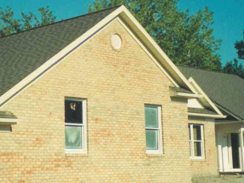 The same gable in 1999 from closer in, two windows set in a field of pale cream brick, a new concrete walk and bare earth at the foot of the wall