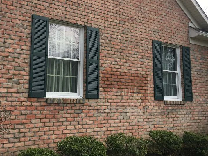 The side wall in 2021 during a water test, a damp patch between the two windows wetting the stained brick the same as the brick around it