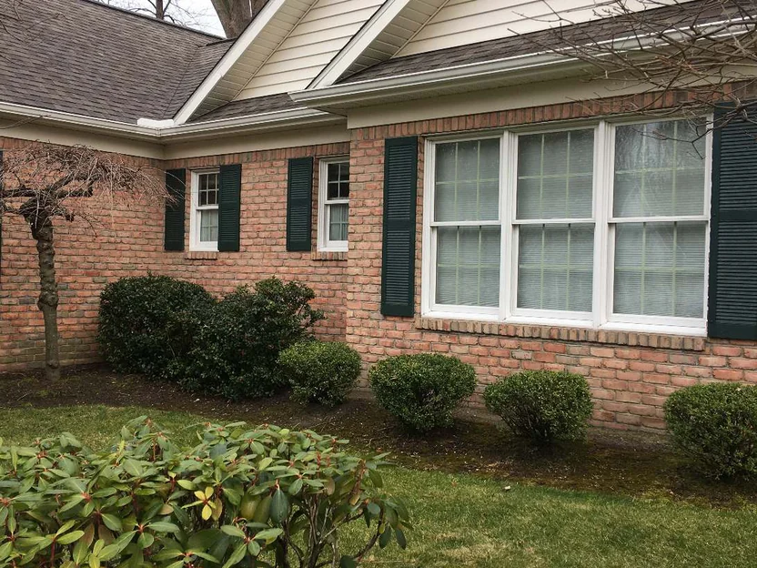 The front of the house in 2021, red brick running level under the eaves past three windows with dark green shutters