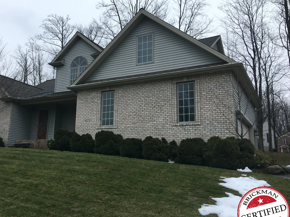 The front of a two-story home in Erie in 2020, buff brick across the gable wing and the entry under grey siding