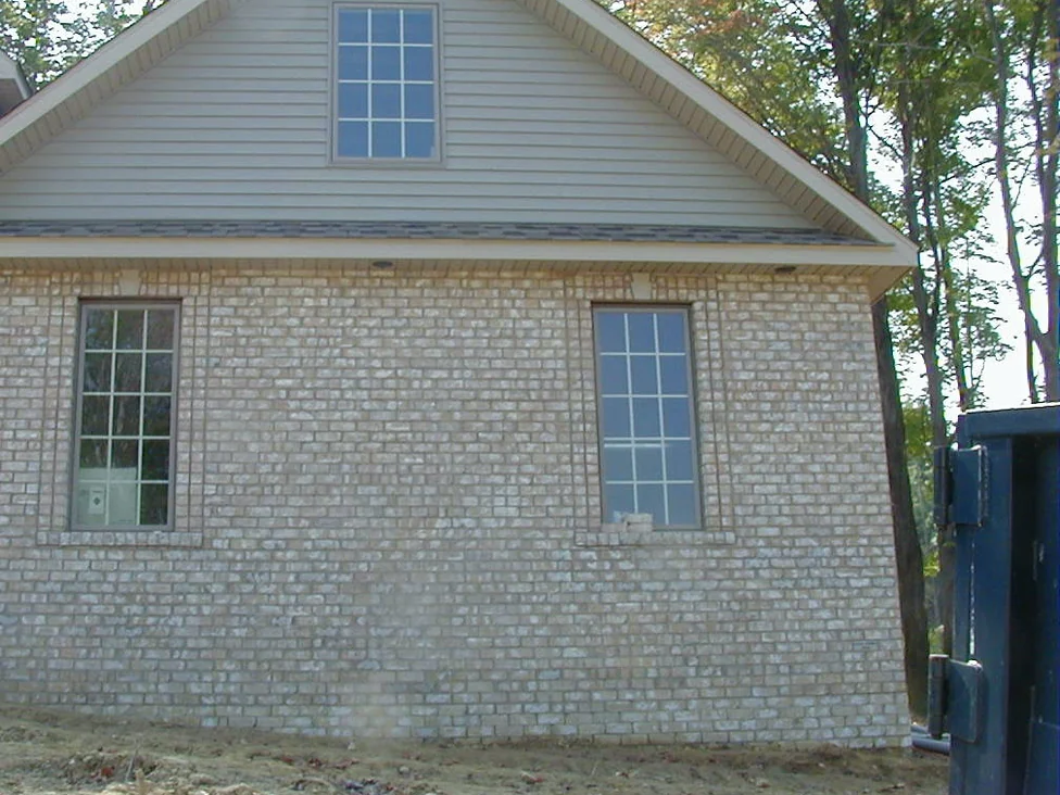 The same side wall in 2004 after staining, the brick reading as one warm buff range between the two windows, with a dumpster at the right edge
