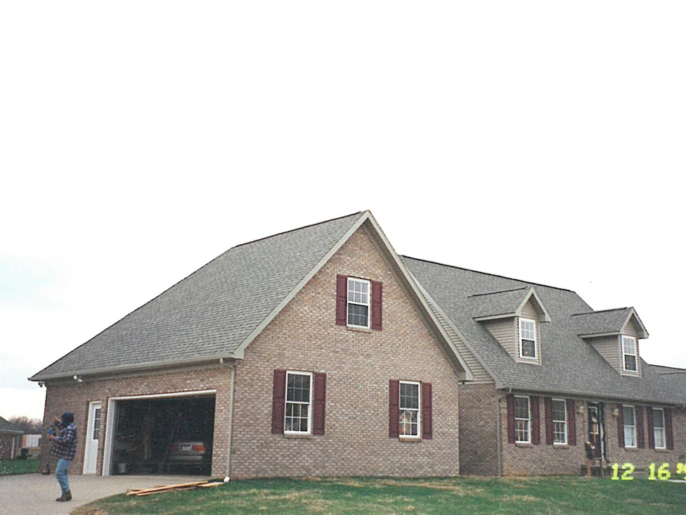 The house from the driveway in 1998, the garage wing, the dormers and the entry all in the same pale tan brick, with no planting on the lot