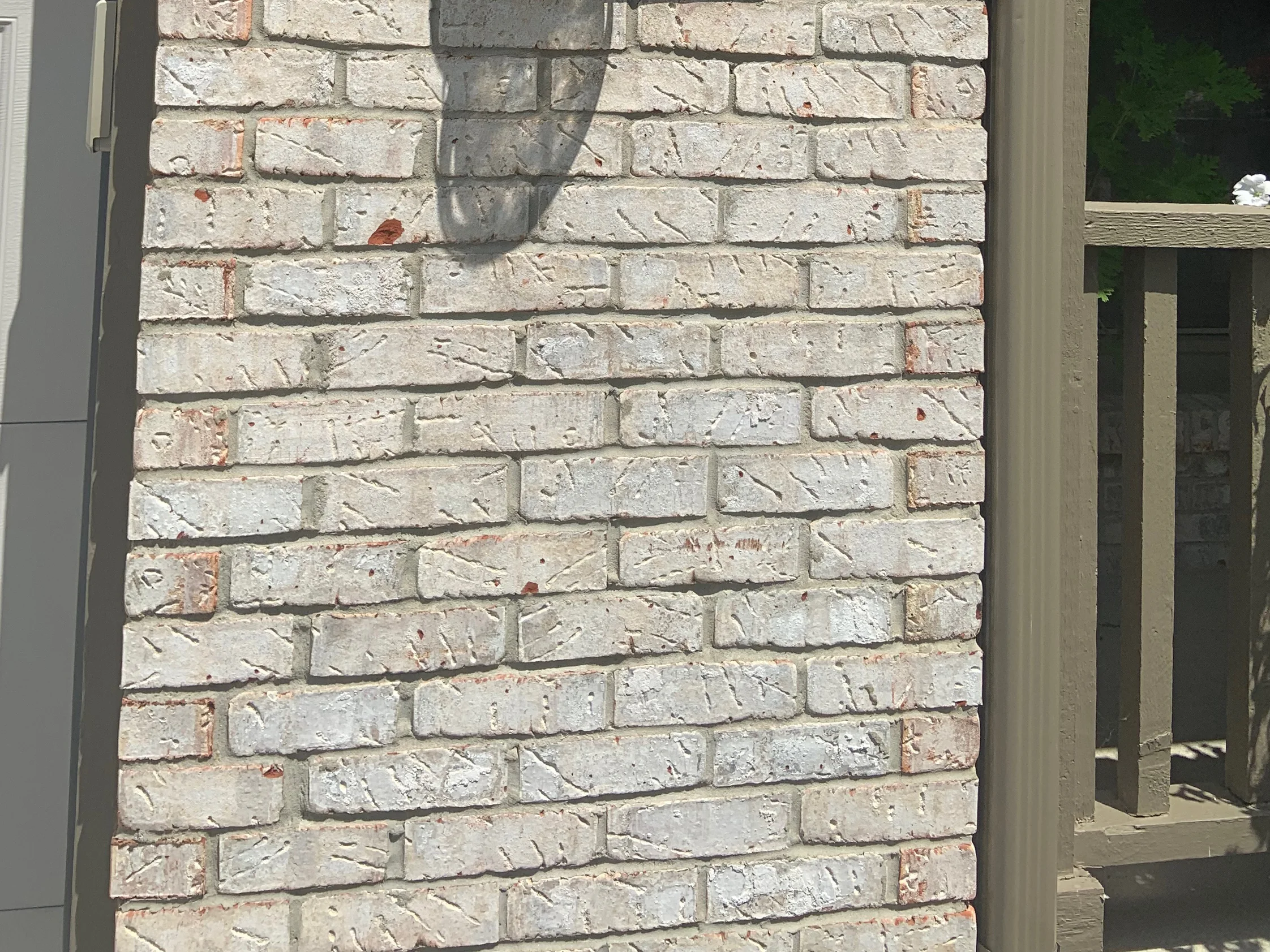 The brick at unit scale in 2019, pale grey and cream units with red flecks and wide grey mortar joints, on a pier between the garage door and the porch