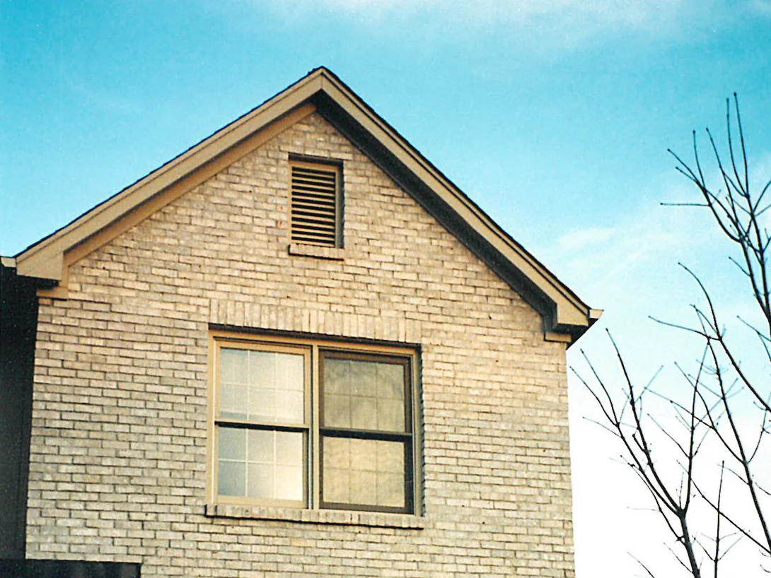 The gable end of the house in low winter sun in 1998, an attic vent in the peak above an upper window with no shutters, the brick one buff range