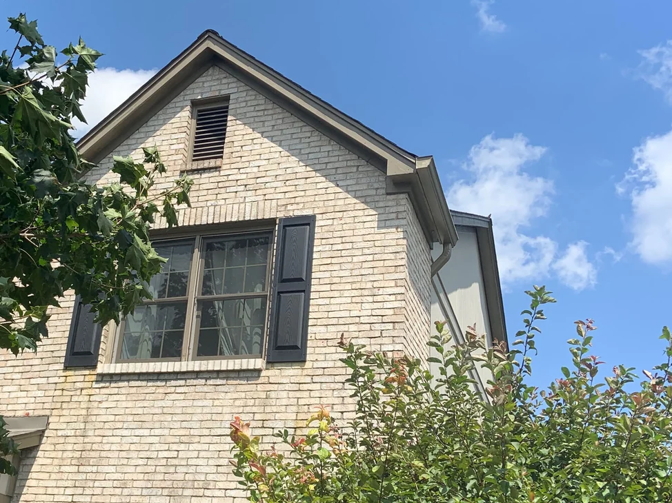 The gable end of a Fishers house in 2019, the attic vent in the peak above a shuttered upper window, the brick an even cream and buff range.
