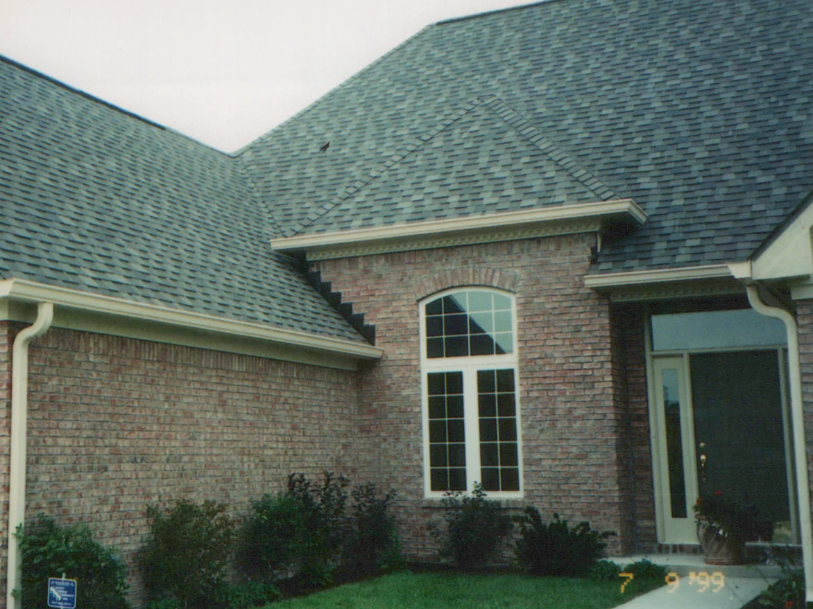 The entrance side of the house in 1999 under a grey shingle roof, the side wall and the window bay reading as one range of red and tan brick, with a 7 9 '99 camera date in the corner