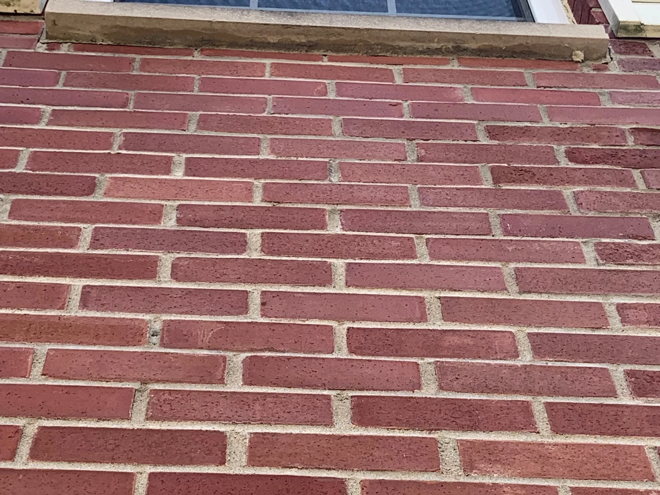 Close view of the wall under a cast stone sill in 2019, the units a deep red across the whole course and sandy tan mortar in every joint
