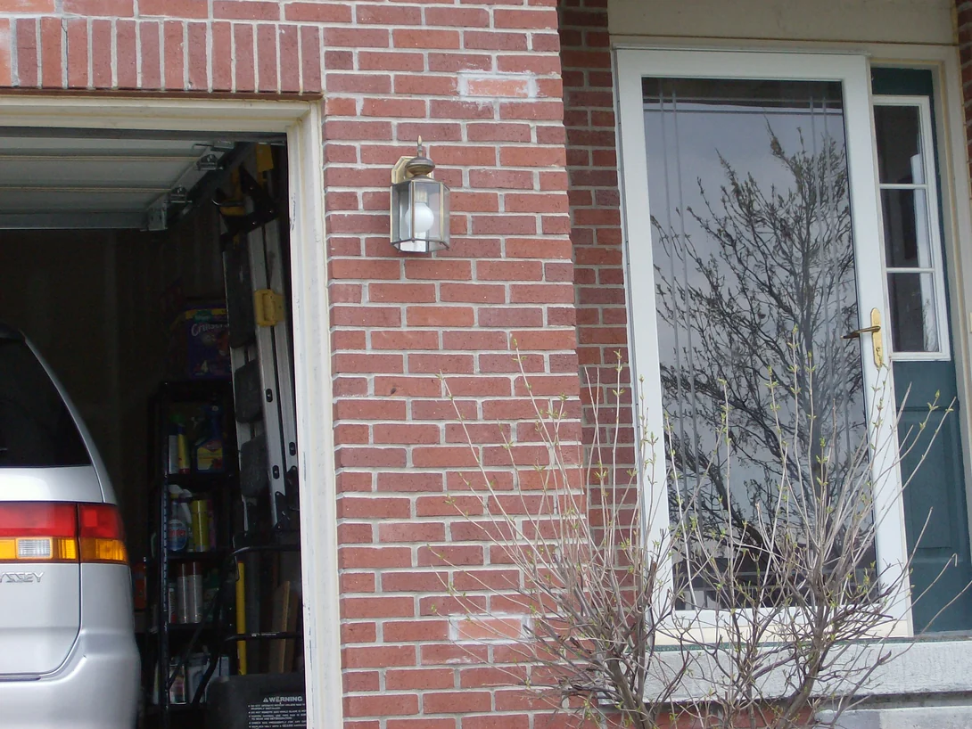 The front entrance in 2007, a brass lantern mounted on pale red brick between the garage opening and the storm door, every joint bright white