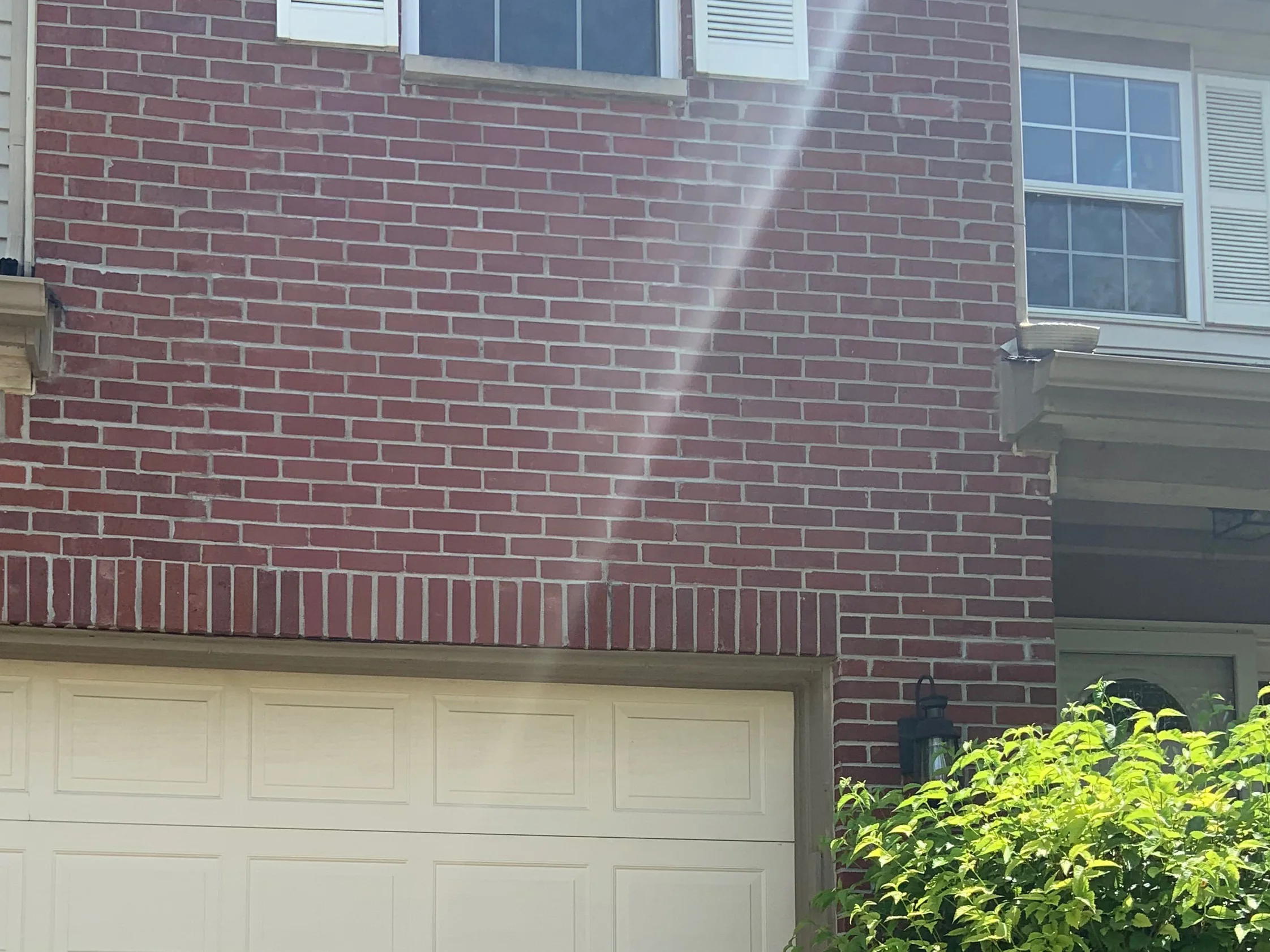 The house from the driveway in 2019, two storeys of deep red brick standing over the garage door with the entrance alcove and a shrub to the right
