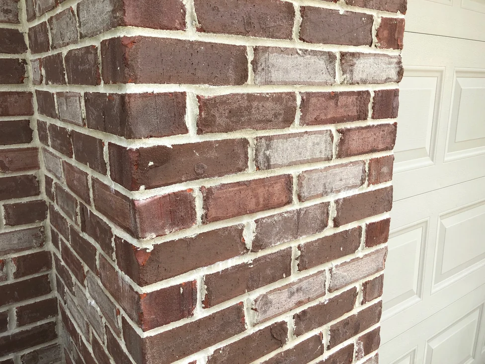 Close view of the brick at an outside corner in 2019, dark maroon units set among lighter grey and tan ones with pale sandy joints