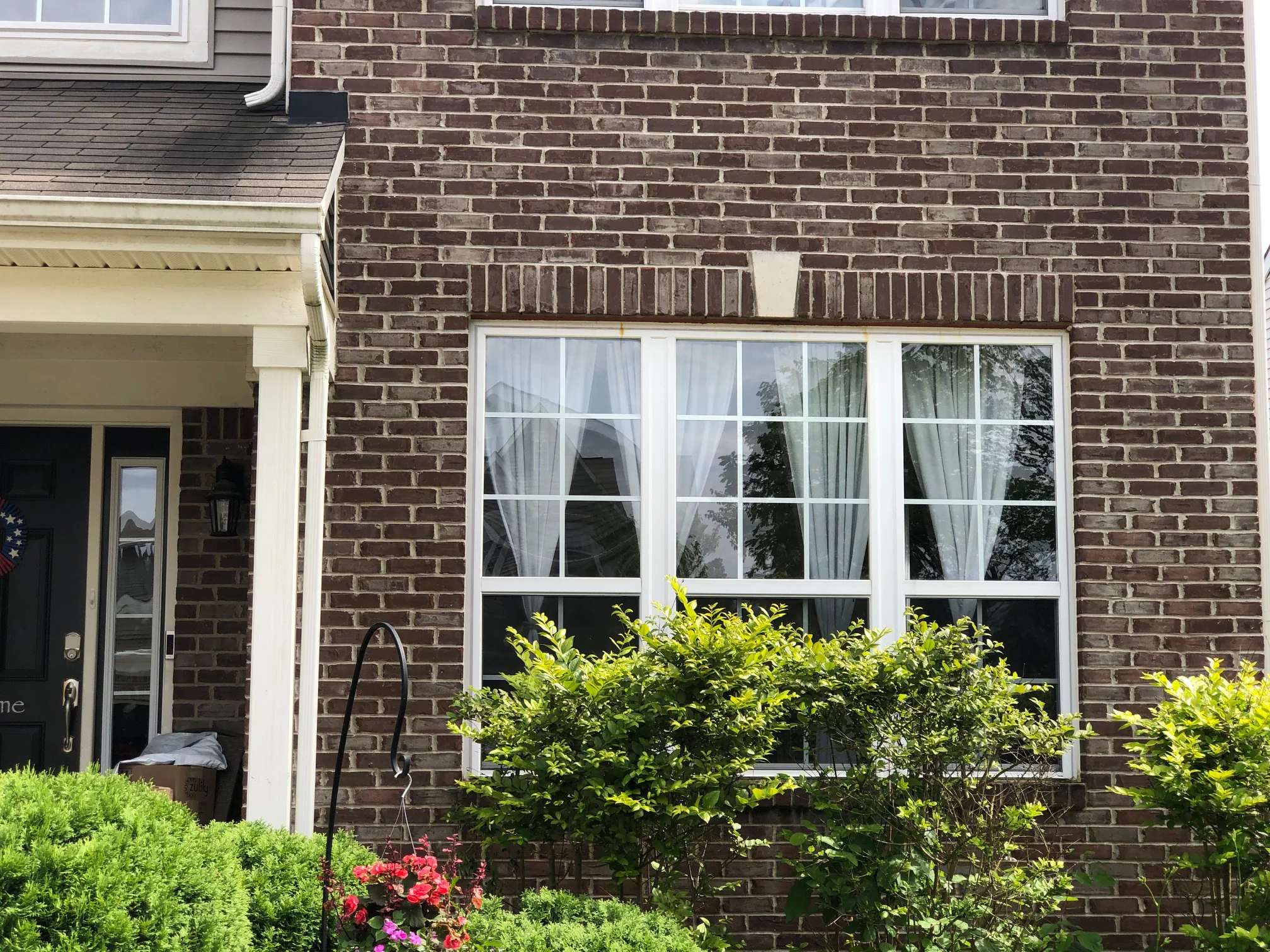 The front entrance and the bay window in 2019, the brick an even dark red and brown range with shrubs grown up under the sill