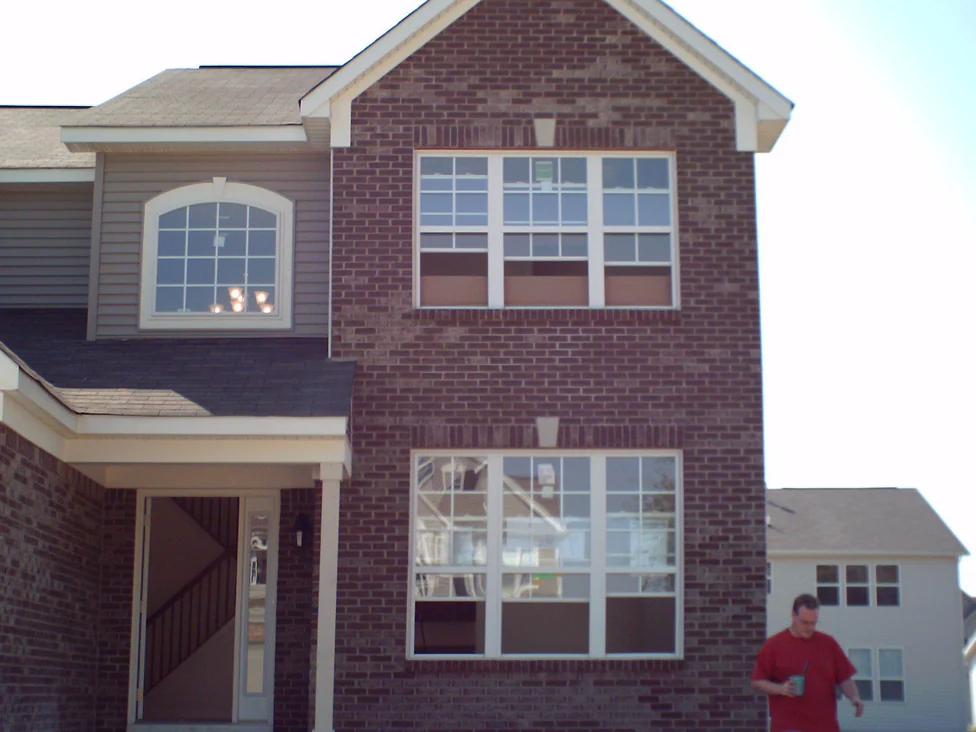 The front of the two-story house in 2008 with the work under way, deep maroon brick beside tan siding, a white porch post and an arched upper window
