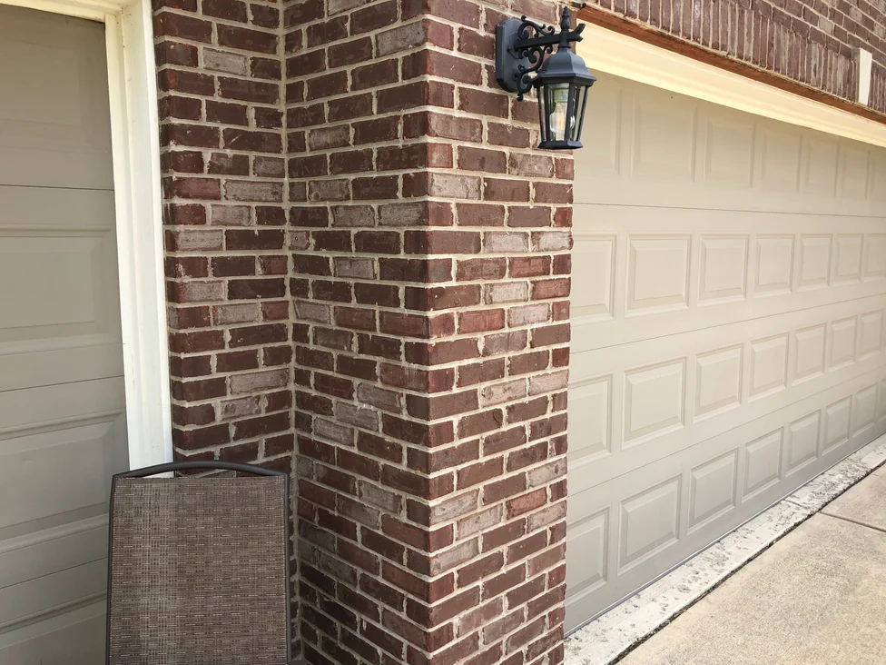 The brick pier between the two garage bays in 2019, a black coach lamp mounted on it and the wall returning around the outside corner