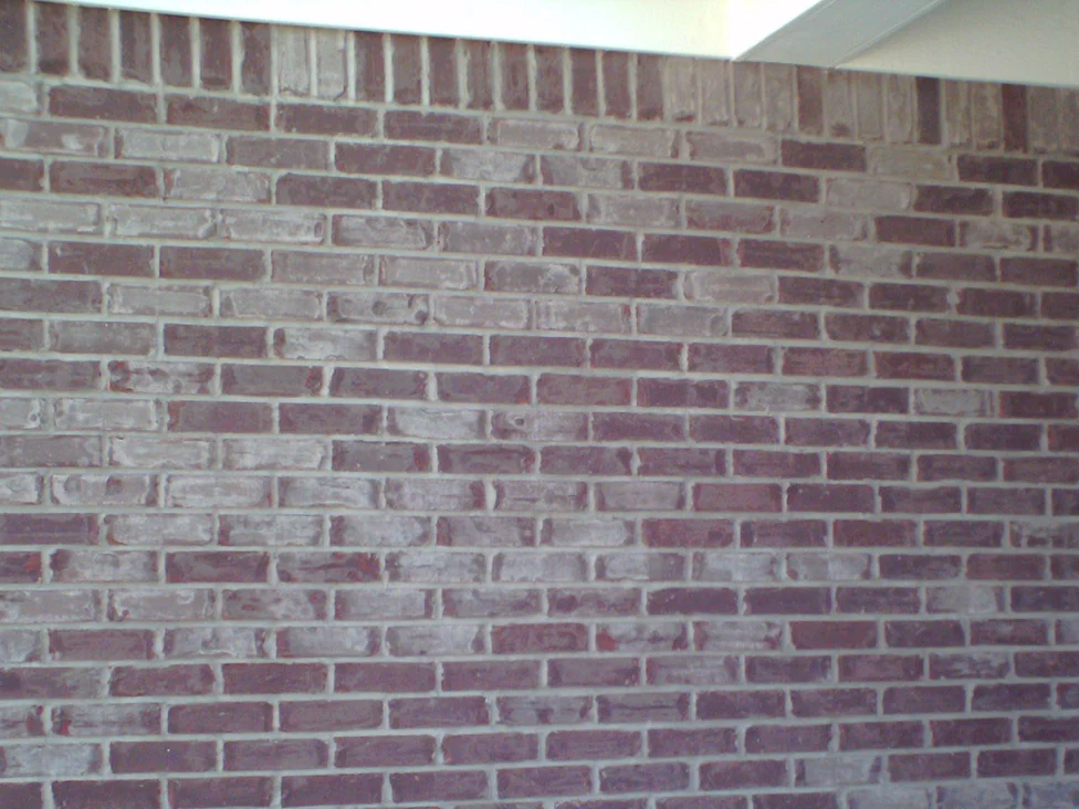 A brick wall in 2008, pale grey and washed out units sitting among dark maroon ones under a soldier course and a white soffit