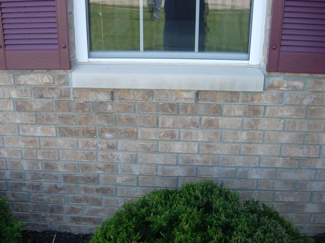 Close view under a cast stone window sill in 2007, the brick below the sill a grey brown that does not match the buff units either side of the opening