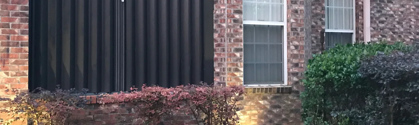 The stained addition wall of the Florida house in 2021, its brick running in the same brown and tan blend as the original walls behind a row of shrubs