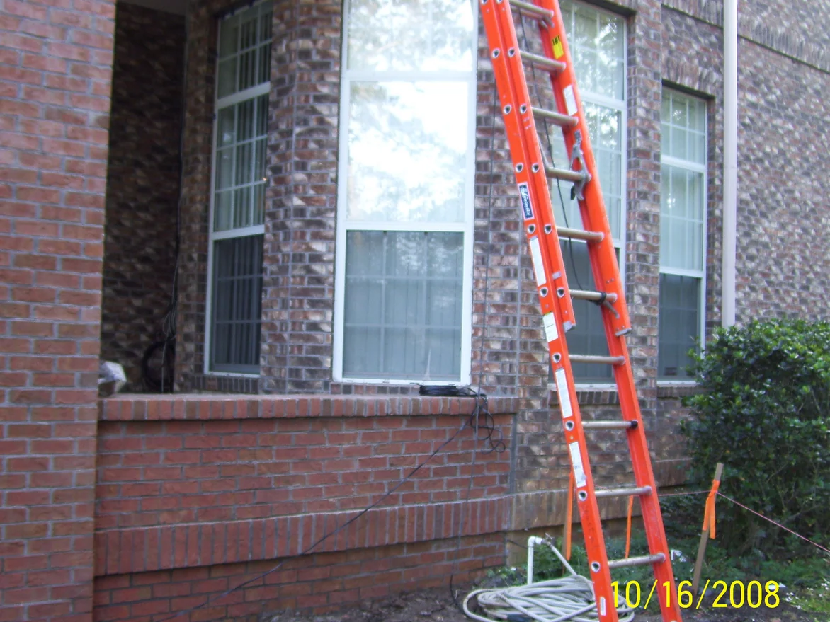 The corner of the Florida house in October 2008, a pier and low wall of plain red brick standing against the mottled brown and tan blend of the original walls, with an extension ladder leaning beside the windows