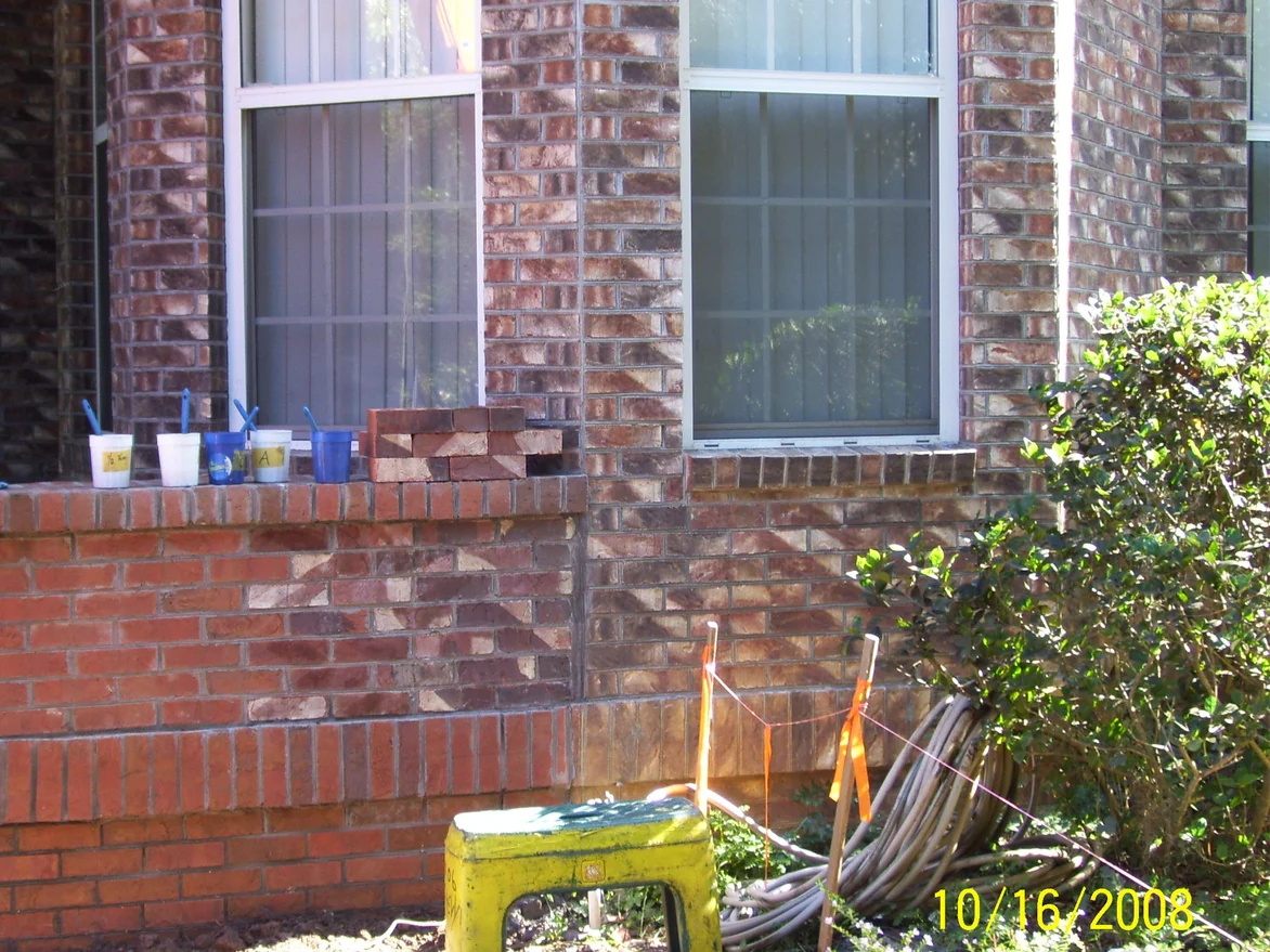 The low wall in October 2008 with labelled mixing cups and brushes set along its cap beside a stack of loose bricks, the red units below already carrying darker and lighter tones