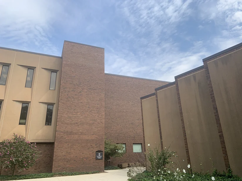 Neff Hall from its courtyard walk in 2019, a brick stair tower carrying the building sign between two rendered wings.