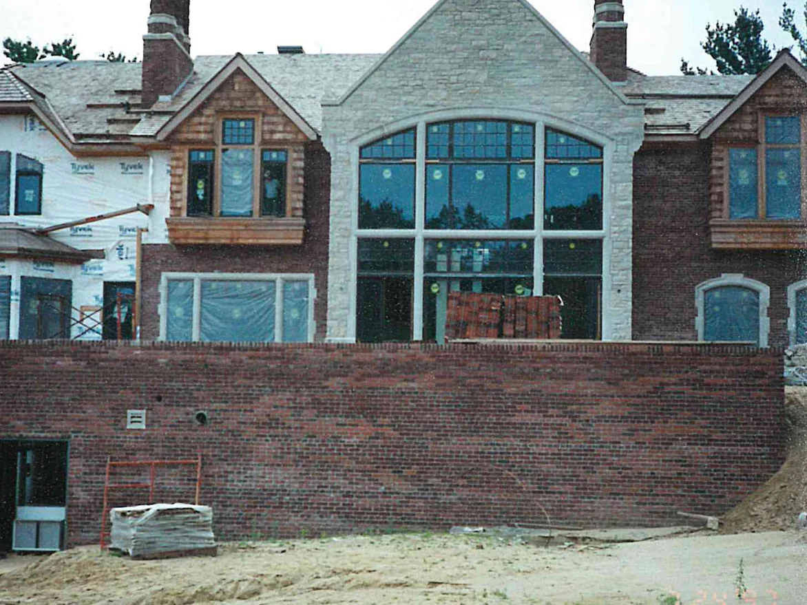 The rear of the house under construction in 1997, seen across the brick terrace wall, with a stack of brick standing on the floor behind the arched window