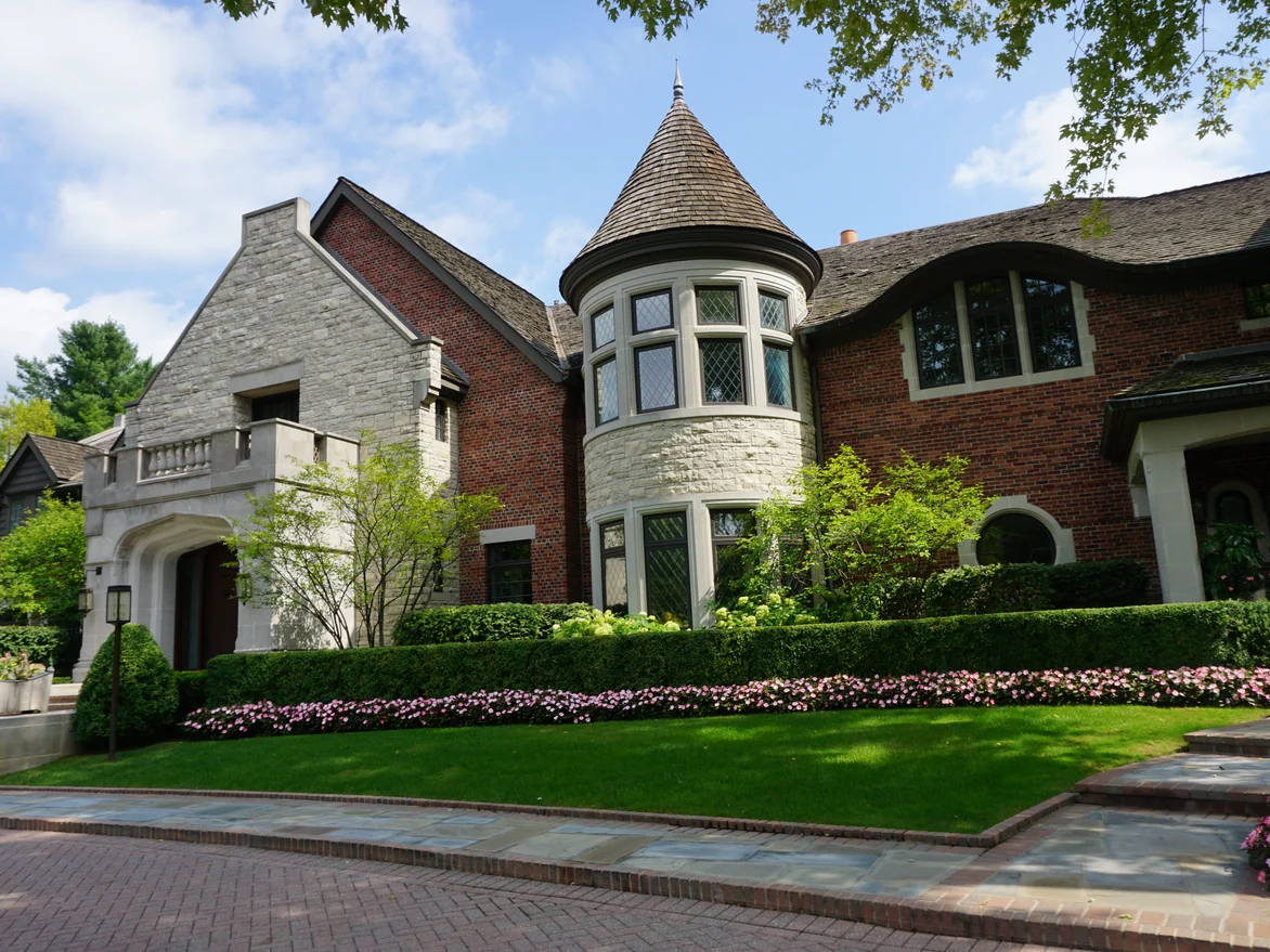 The front of the house in 2019, a round bay under a conical shingled roof set between a limestone gable and brick walls