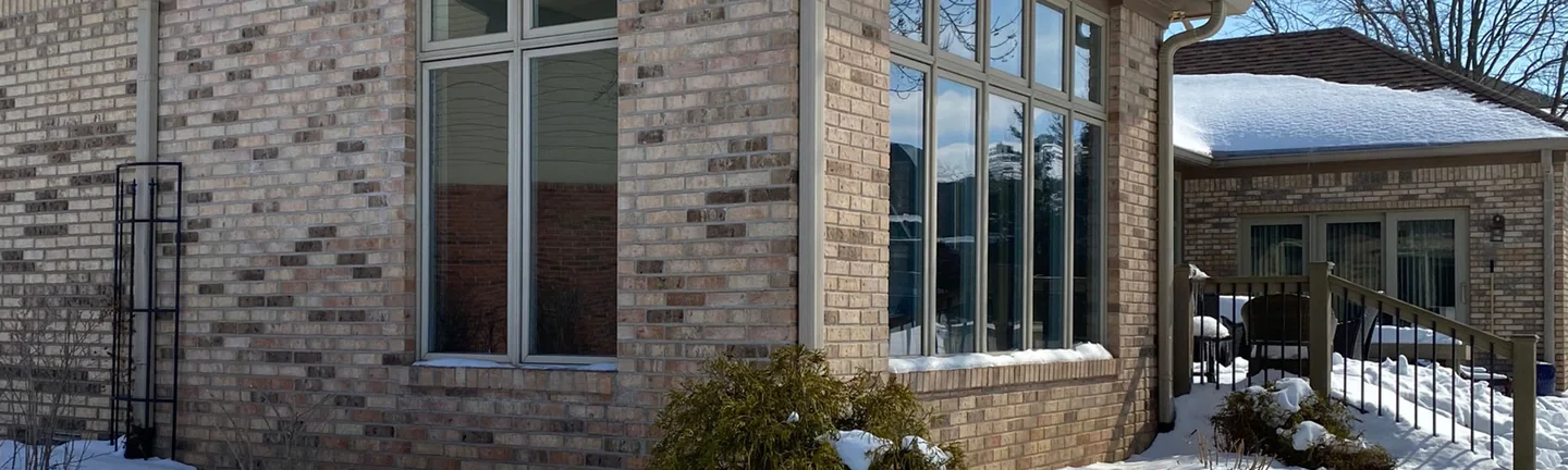 The corner of the addition in 2021, tan and brown blended brick running from the house wall across the corner pier to a bank of windows