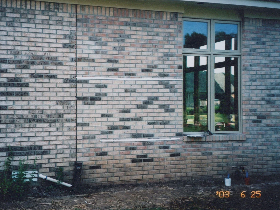 The addition wall in June 2003 beside the original house wall, a vertical seam between the two bricks left of center, two strips of white tape across the new brick and a burned-in camera date in the corner