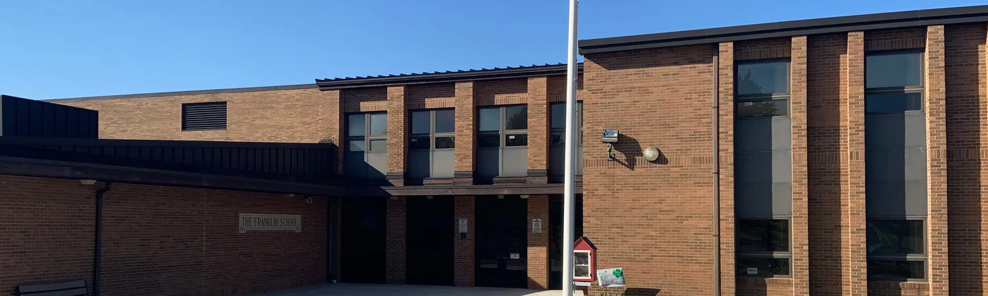 The front of the Franklin School in 2019, its classroom wing and low entrance range reading as one even red brown brick